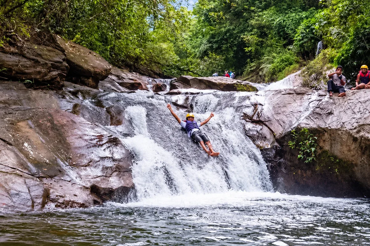 A visitor wearing a helmet and life jacket sliding down a rocky cascade into a pool