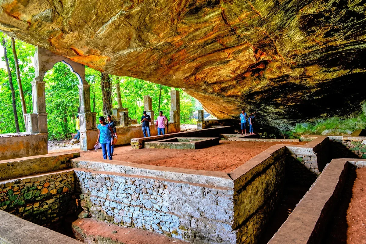 Visitors exploring stone structures beneath a large rock overhang