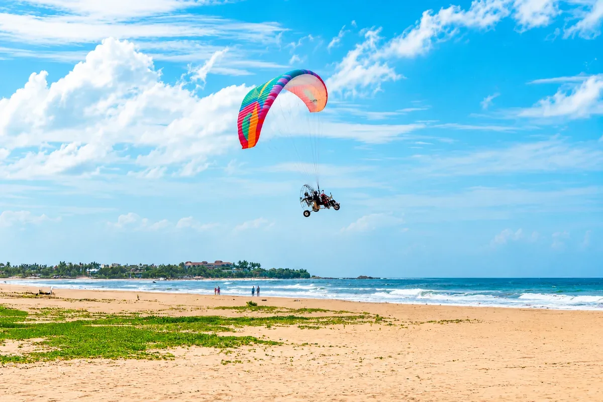 A powered paraglider flying above a sandy beach