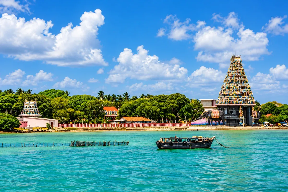 A colourful Hindu temple beside turquoise water with a boat in the foreground