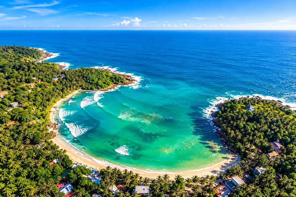 Aerial view of Hiriketiya bay with turquoise water, a curved sandy beach and palm trees