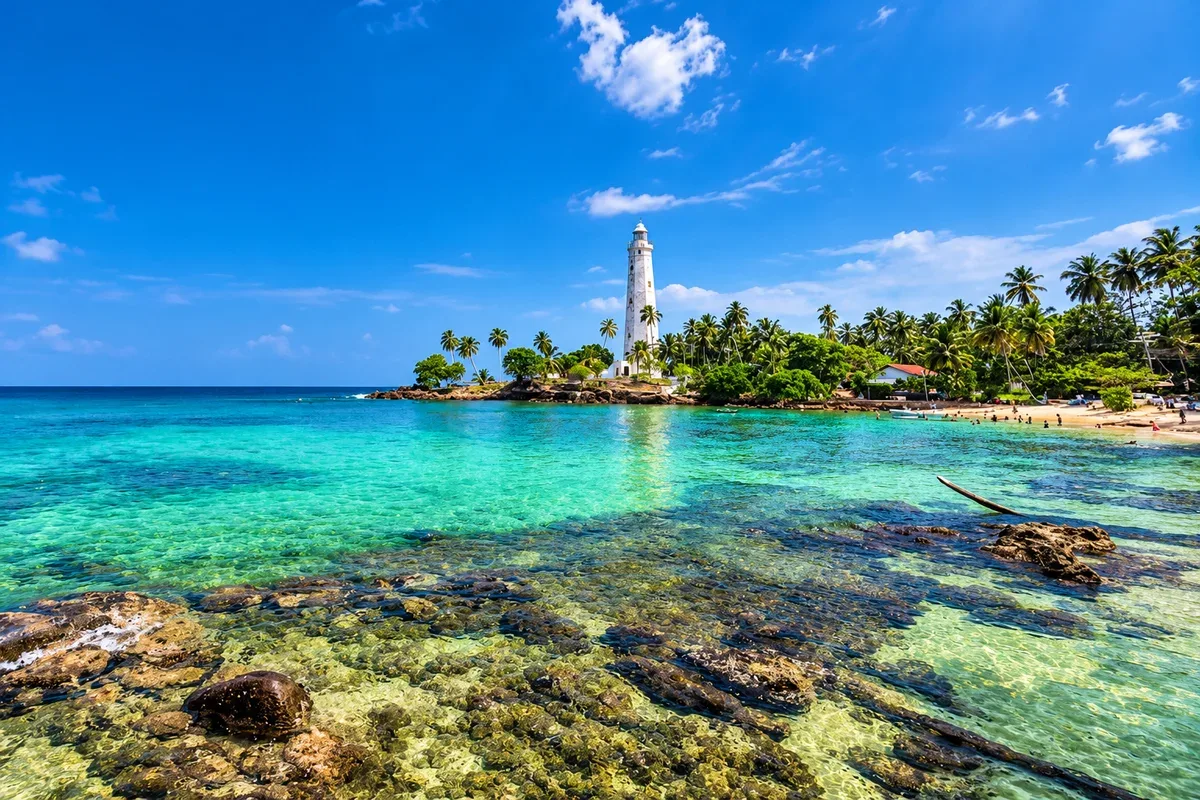 A white lighthouse beside palm trees and clear coastal water